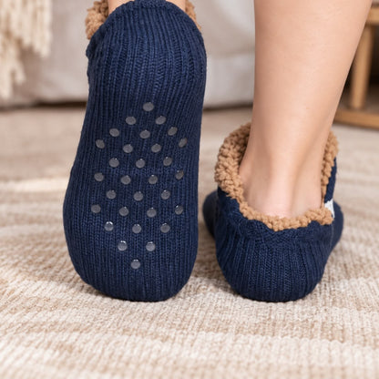 Sohle einer blauen Haussocke mit grauen Silikonnoppen, dahinter ein zweiter getragener Socken auf Teppichboden