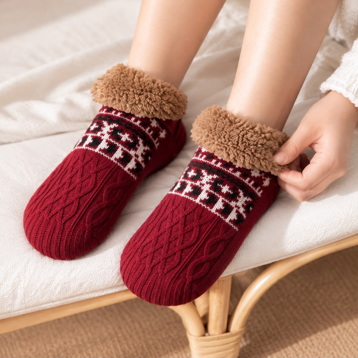 Weinrote Haussocken an den Füßen einer sitzenden Person, eine Hand streift den Teddybund um